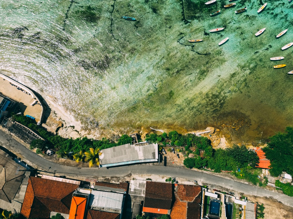 Aerial view of the coastal road and rooftops above the seaweed-farm shallows on Nusa Ceningan